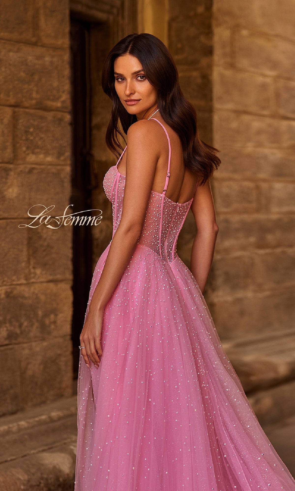 A woman poses in front of a stone wall, looking over her shoulder in the Pearl Classic Long Prom Dress: La Femme 32644, a strapless A-line gown featuring a fitted bodice and flowing skirt adorned with pearl beading.